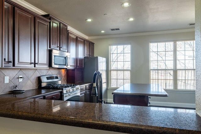 kitchen featuring crown molding, dark stone countertops, stainless steel appliances, tasteful backsplash, and dark brown cabinetry