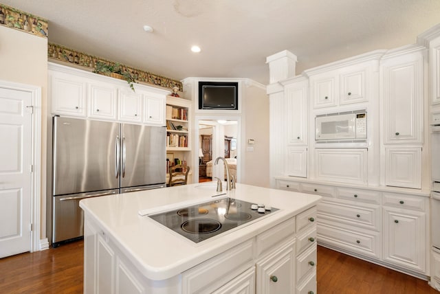 kitchen with stainless steel fridge, a kitchen island with sink, white microwave, black electric stovetop, and dark hardwood / wood-style flooring