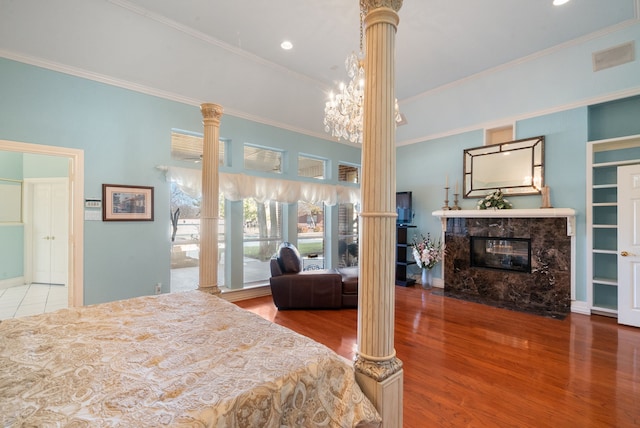 bedroom featuring crown molding, hardwood / wood-style floors, a notable chandelier, a high end fireplace, and ornate columns