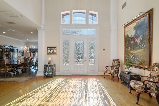 entrance foyer featuring hardwood / wood-style flooring, a towering ceiling, crown molding, and an inviting chandelier