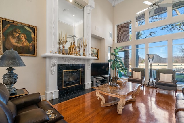 living room with crown molding, a tile fireplace, ceiling fan, a high ceiling, and wood-type flooring