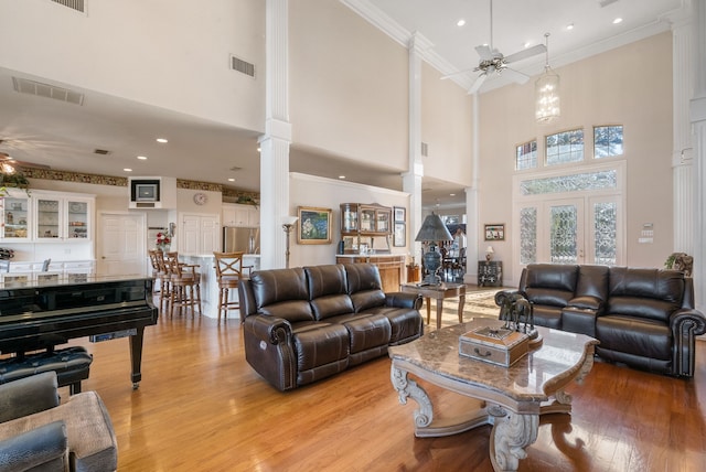 living room featuring decorative columns, crown molding, ceiling fan, and light wood-type flooring