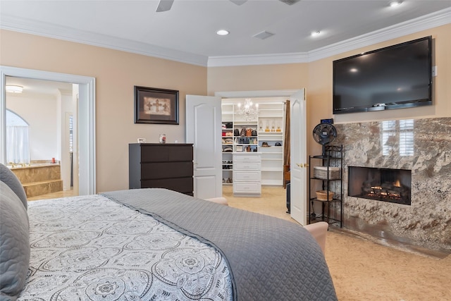 bedroom with ornamental molding, a walk in closet, light colored carpet, ceiling fan, and a premium fireplace