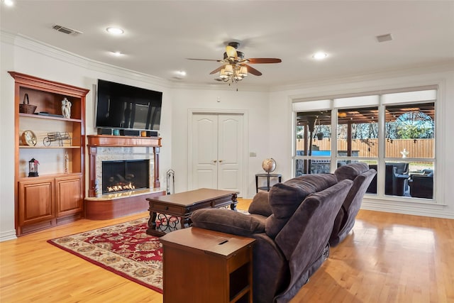 living room with crown molding, ceiling fan, and light wood-type flooring