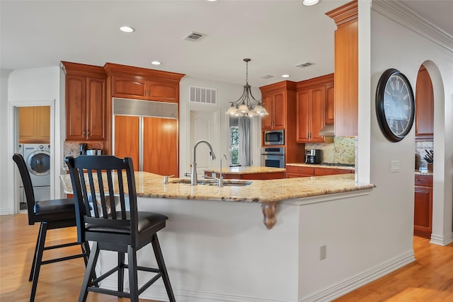 kitchen featuring built in appliances, sink, washer / dryer, and kitchen peninsula