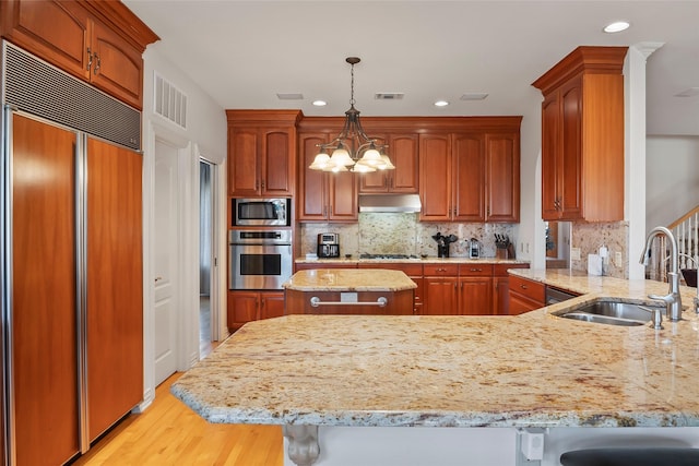 kitchen featuring sink, light stone counters, built in appliances, decorative light fixtures, and kitchen peninsula