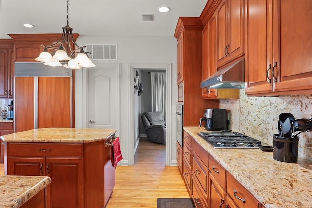 kitchen with pendant lighting, light stone counters, stainless steel appliances, and a kitchen island