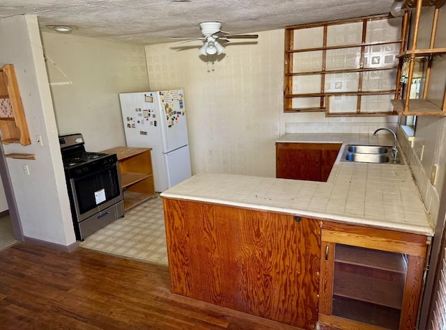 kitchen with sink, stainless steel gas range oven, tile countertops, white refrigerator, and kitchen peninsula