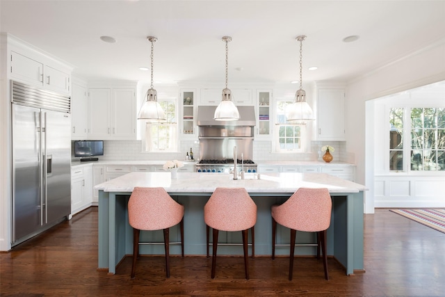 kitchen featuring built in fridge, white cabinetry, a breakfast bar area, and a center island with sink