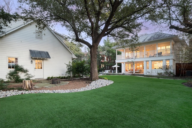 back house at dusk featuring cooling unit, a lawn, and a balcony