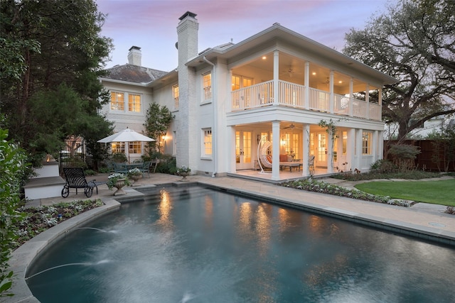 back house at dusk with a patio, a balcony, and ceiling fan