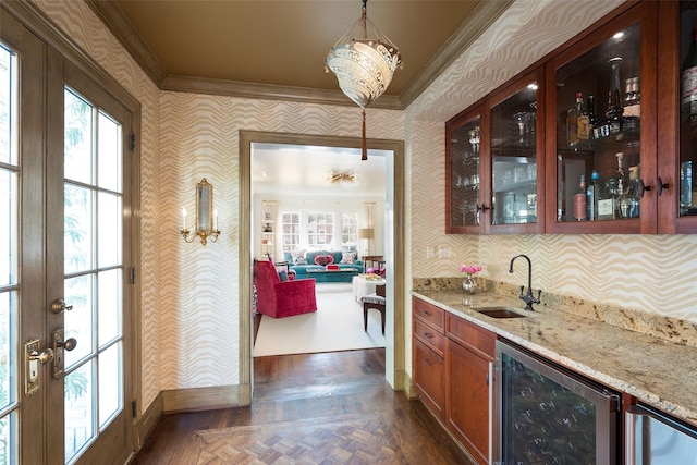 bar with sink, crown molding, hanging light fixtures, light stone counters, and beverage cooler