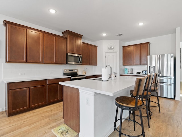 3224 Stillwater Ln, Aubrey, TX 76227 - kitchen with light wood-style flooring, a breakfast bar area, a sink, backsplash, and stainless steel appliances