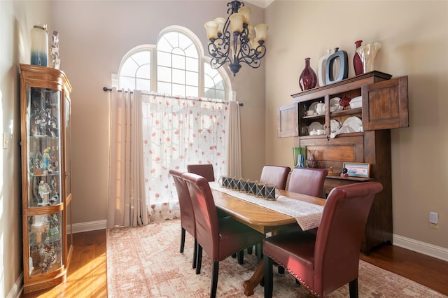 dining space featuring a towering ceiling, wood-type flooring, and a notable chandelier