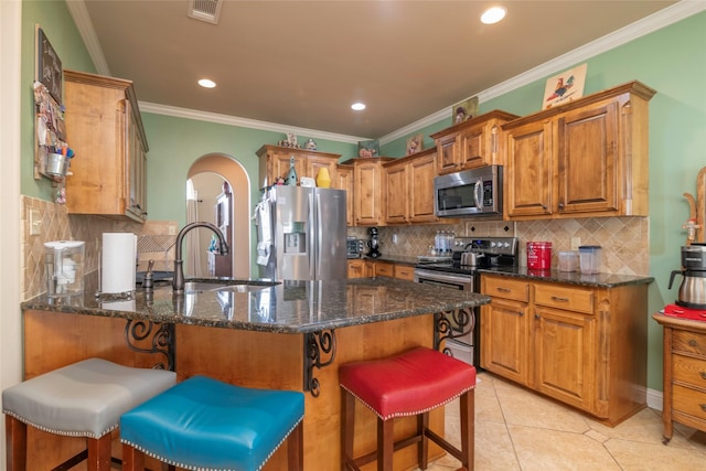 kitchen featuring appliances with stainless steel finishes, a kitchen breakfast bar, sink, and dark stone counters