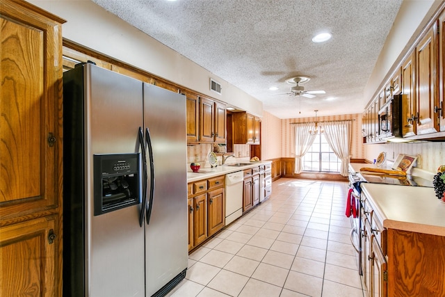 kitchen with light tile patterned floors, ceiling fan with notable chandelier, appliances with stainless steel finishes, a textured ceiling, and decorative light fixtures