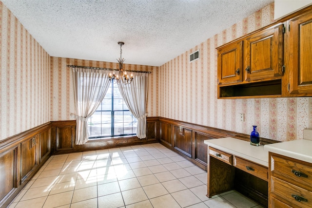 unfurnished dining area with light tile patterned flooring, a notable chandelier, and a textured ceiling