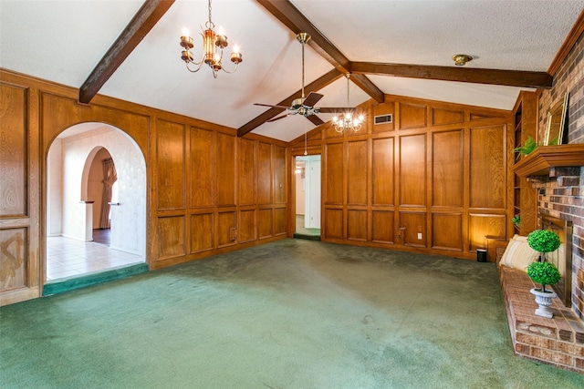 unfurnished living room with wooden walls, dark colored carpet, lofted ceiling with beams, a brick fireplace, and ceiling fan with notable chandelier