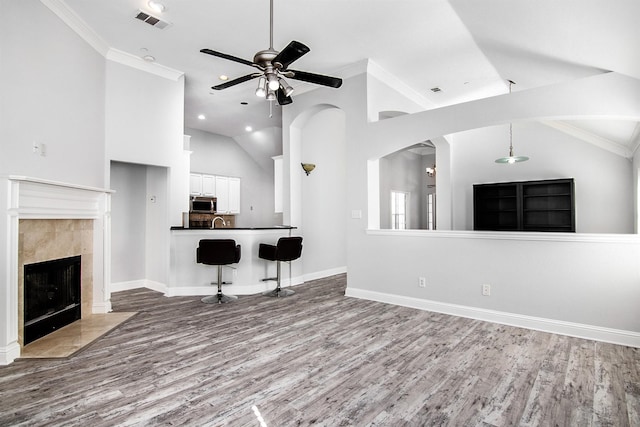 unfurnished living room with a tiled fireplace, wood-type flooring, ornamental molding, and ceiling fan