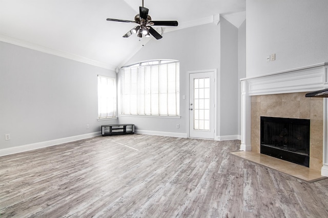 unfurnished living room with ceiling fan, ornamental molding, a tile fireplace, and light wood-type flooring