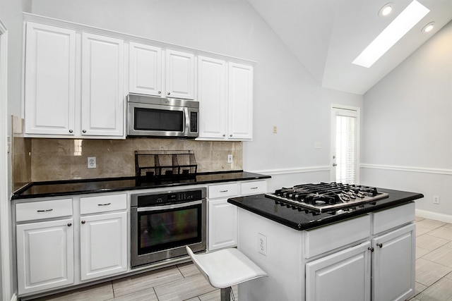 kitchen with a kitchen island, appliances with stainless steel finishes, vaulted ceiling with skylight, and white cabinets