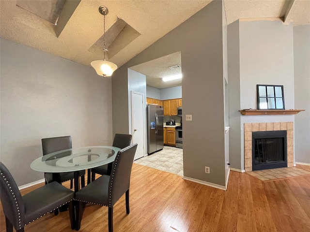 dining space with light hardwood / wood-style flooring, a tile fireplace, a textured ceiling, and vaulted ceiling