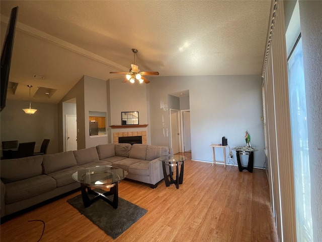 living room featuring lofted ceiling, a textured ceiling, light wood-type flooring, ceiling fan, and a tiled fireplace