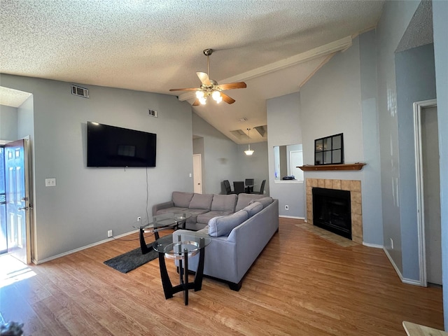 living room with high vaulted ceiling, a tiled fireplace, ceiling fan, a textured ceiling, and light hardwood / wood-style flooring