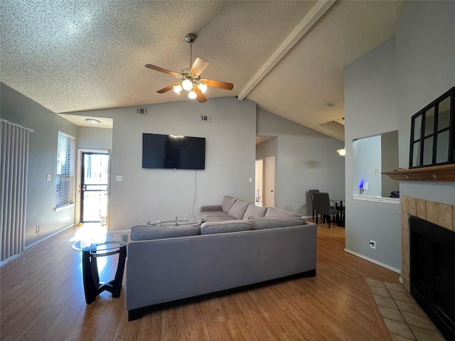 living room with lofted ceiling with beams, wood-type flooring, a tiled fireplace, and a textured ceiling