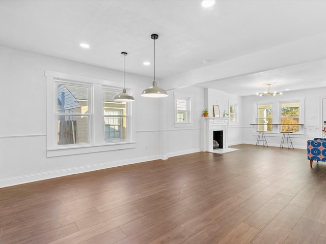 unfurnished living room with an inviting chandelier, plenty of natural light, and dark hardwood / wood-style floors