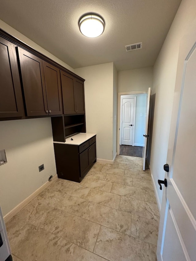 washroom with electric dryer hookup, cabinets, and a textured ceiling