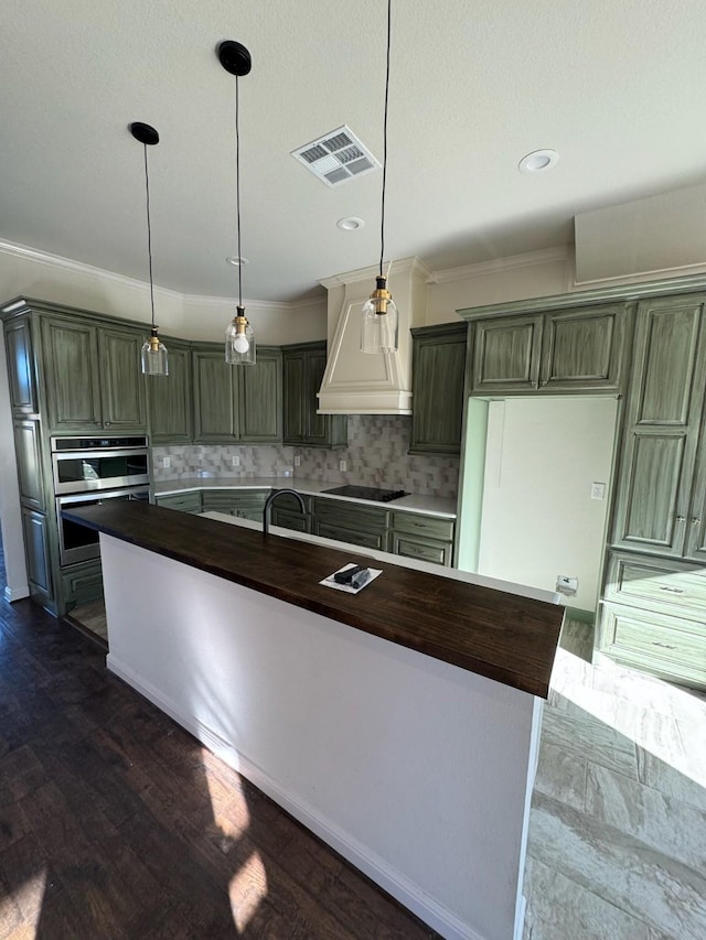 kitchen featuring hanging light fixtures, premium range hood, a kitchen island with sink, and black electric stovetop