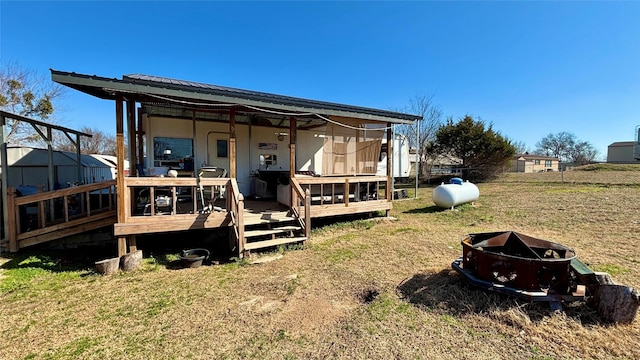 rear view of house featuring a wooden deck, a lawn, and an outdoor fire pit