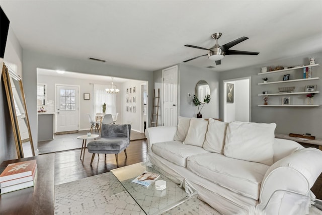 living room with ceiling fan with notable chandelier, visible vents, baseboards, and wood finished floors