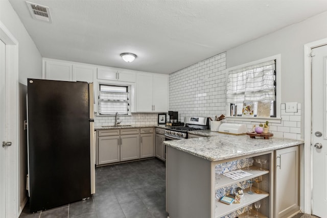 kitchen with a peninsula, a sink, visible vents, stainless steel gas range, and freestanding refrigerator