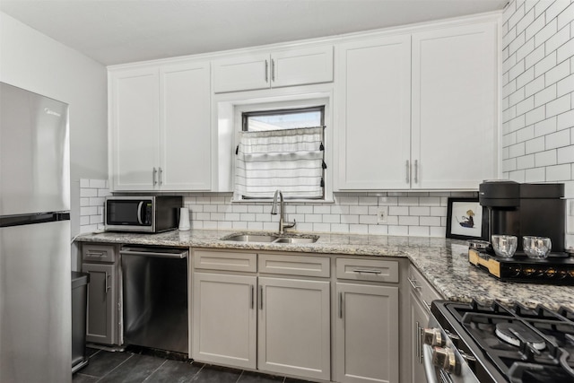 kitchen featuring stainless steel appliances, a sink, white cabinetry, light stone countertops, and tasteful backsplash