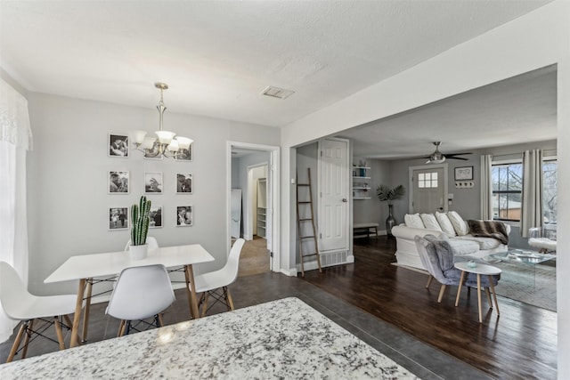 dining area featuring baseboards, visible vents, dark wood-type flooring, a textured ceiling, and ceiling fan with notable chandelier