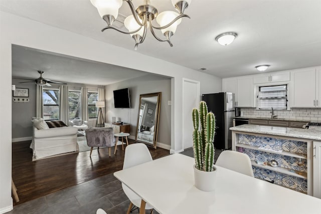 dining space with ceiling fan with notable chandelier, dark wood-style floors, and baseboards