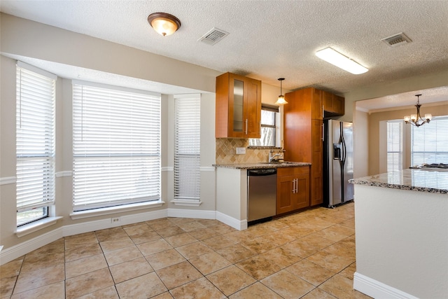 kitchen with pendant lighting, tasteful backsplash, a chandelier, stainless steel appliances, and light stone countertops