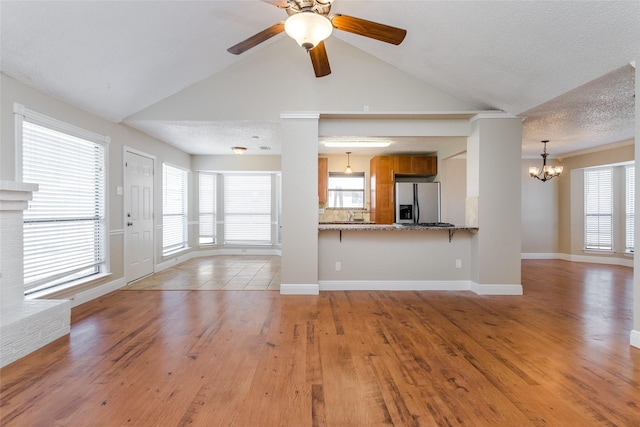 unfurnished living room featuring ceiling fan with notable chandelier, light hardwood / wood-style flooring, and a textured ceiling