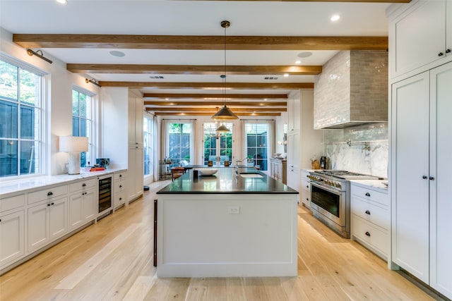 kitchen featuring decorative light fixtures, white cabinets, wine cooler, high end range, and wall chimney exhaust hood