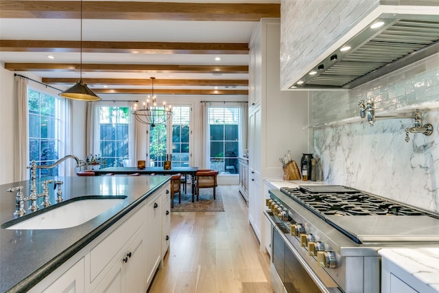 kitchen featuring sink, white cabinetry, stainless steel stove, custom range hood, and dark stone counters