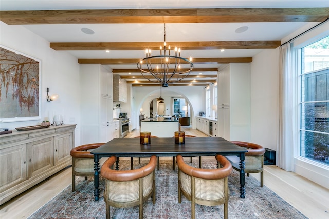 dining space featuring an inviting chandelier, beam ceiling, and light hardwood / wood-style flooring