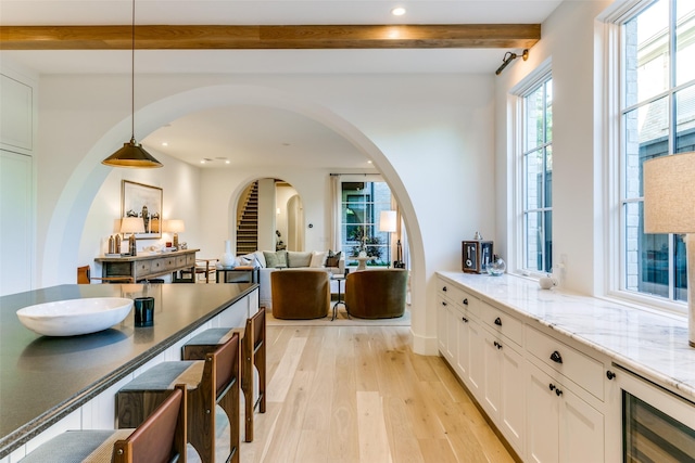 kitchen with decorative light fixtures, wine cooler, white cabinets, light hardwood / wood-style floors, and light stone countertops