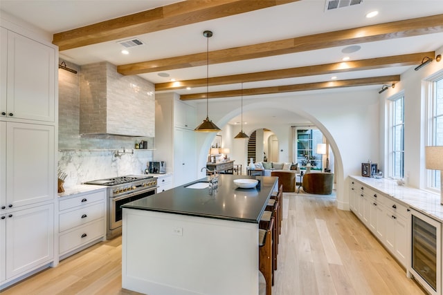 kitchen with pendant lighting, sink, white cabinets, beverage cooler, and range with two ovens