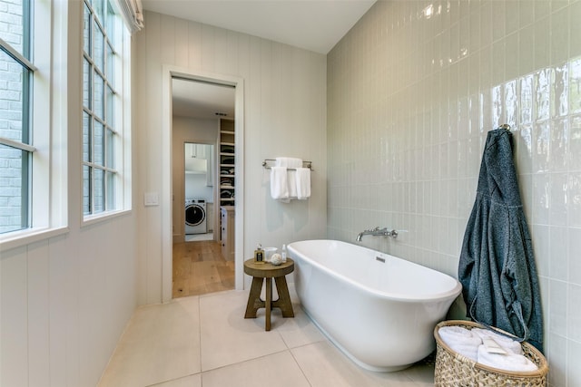 bathroom with washer / clothes dryer, a tub, tile walls, and tile patterned floors