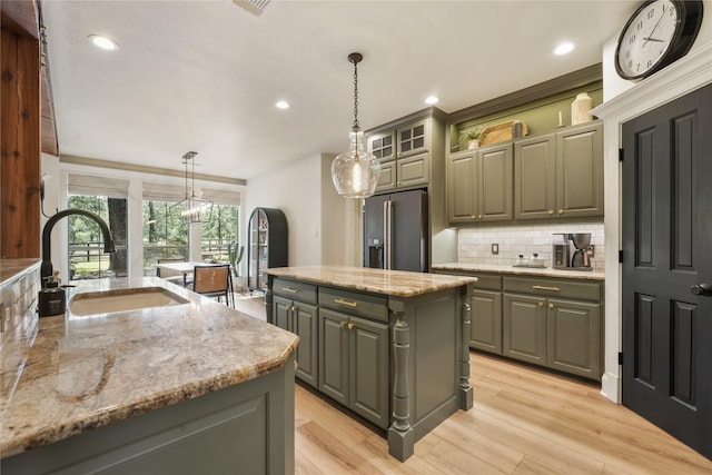 kitchen with sink, gray cabinetry, high quality fridge, pendant lighting, and a kitchen island with sink