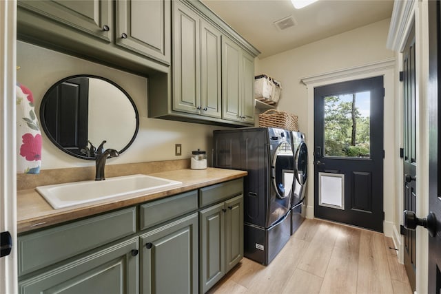 clothes washing area with cabinets, light hardwood / wood-style floors, sink, and washing machine and dryer