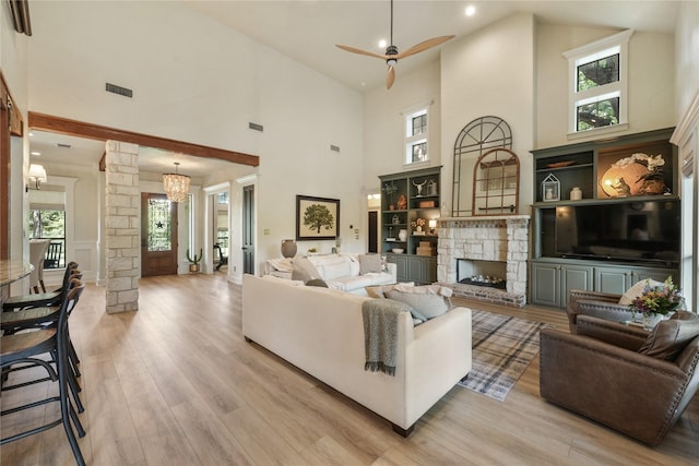 living room with ornate columns, a stone fireplace, a healthy amount of sunlight, and light hardwood / wood-style flooring