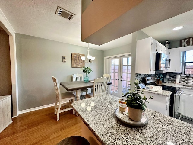 kitchen featuring hardwood / wood-style flooring, appliances with stainless steel finishes, white cabinetry, light stone counters, and french doors